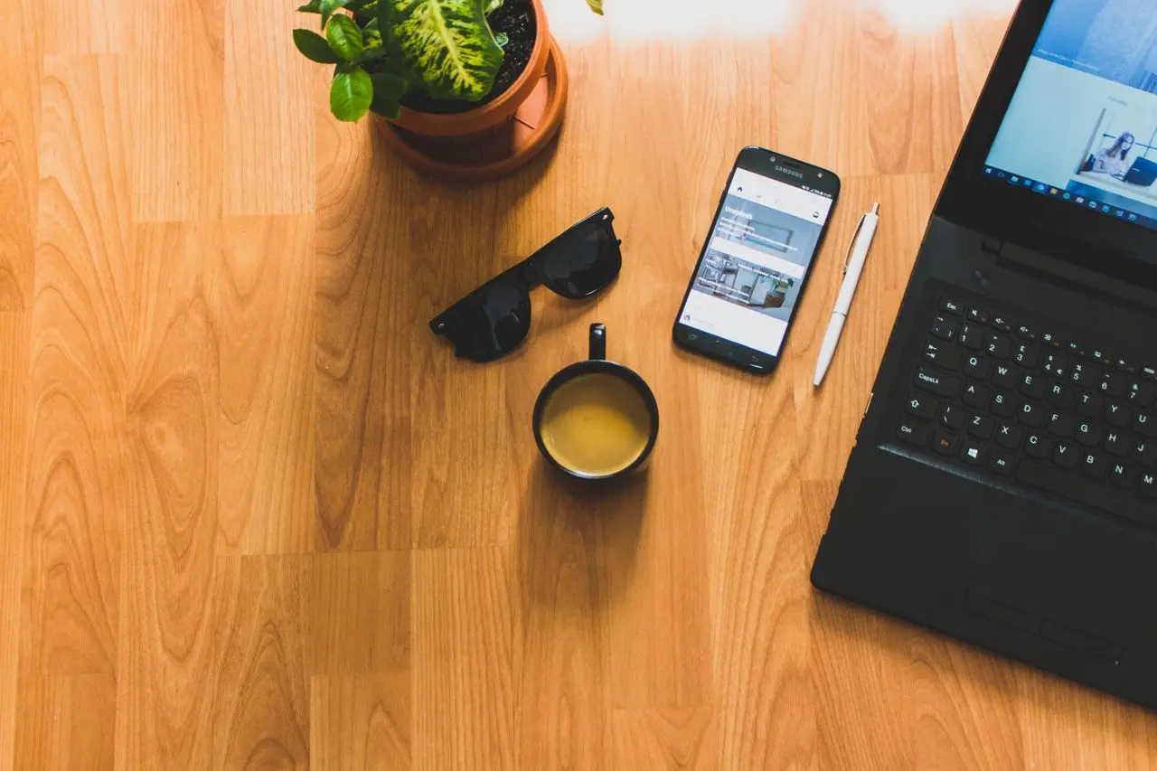Wooden desk with laptop, smartphone, coffee cup, and plant, representing the peace of mind of automatic savings (Photo on Pexels)