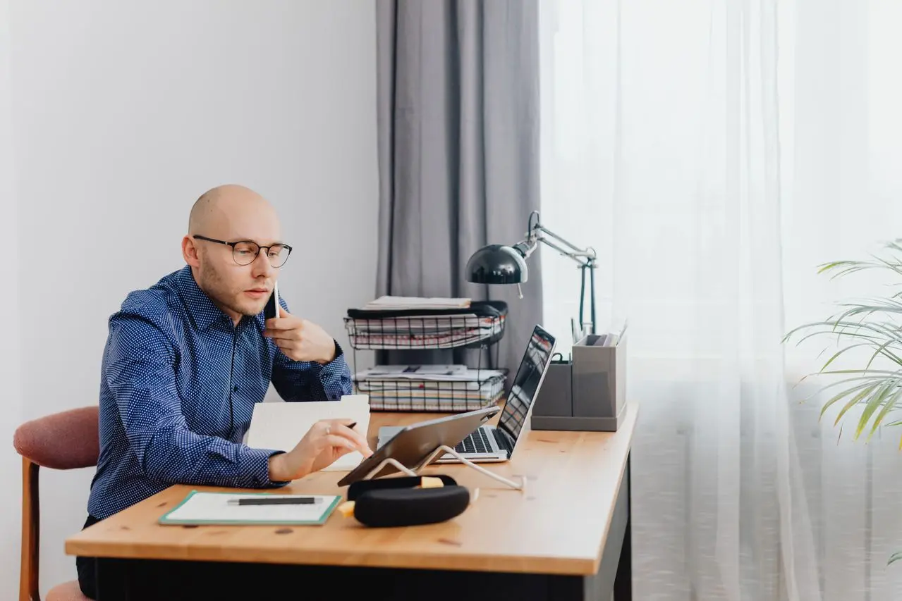 Homme concentré à son bureau examinant ses finances mensuelles sur tablette et ordinateur (Photo sur Pexels)