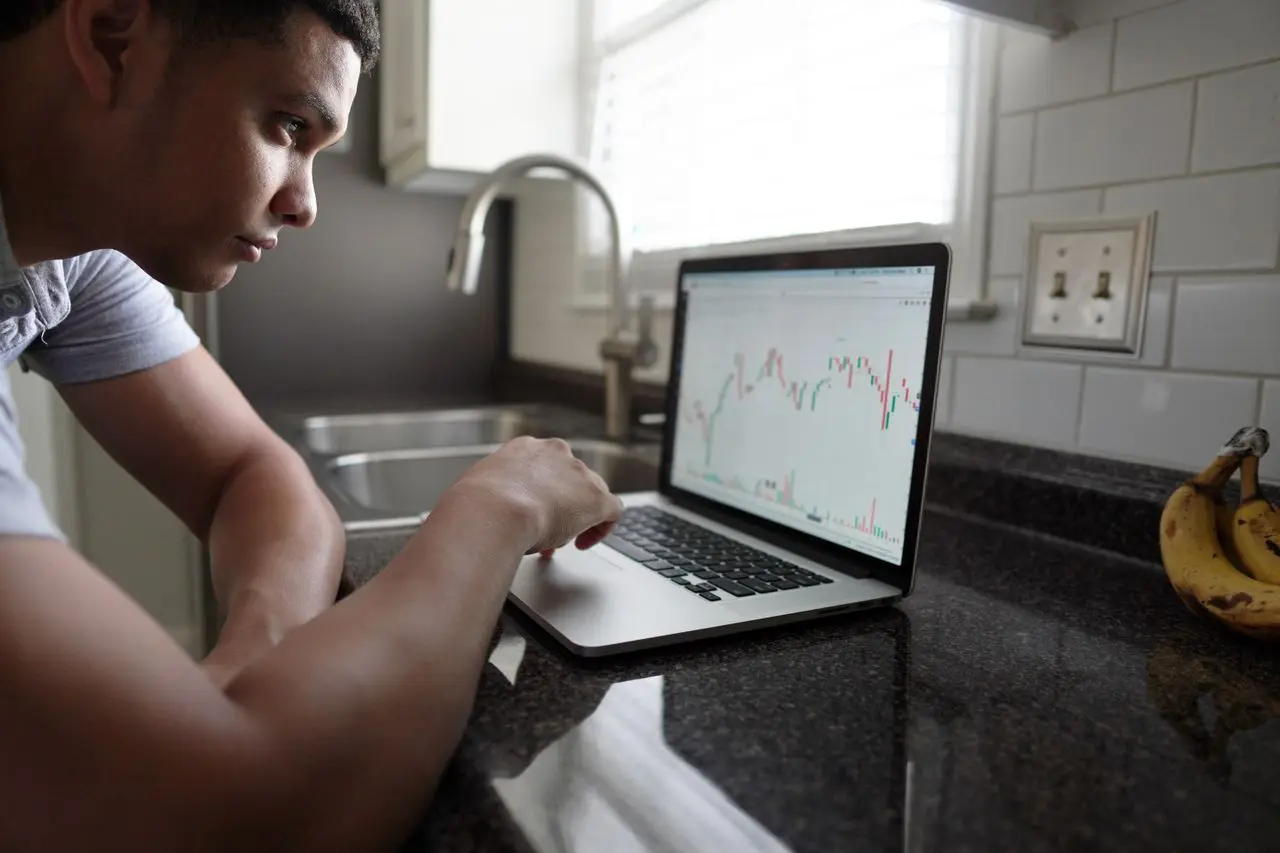 Persona che analizza grafici finanziari e investimenti sul laptop dalla cucina di casa