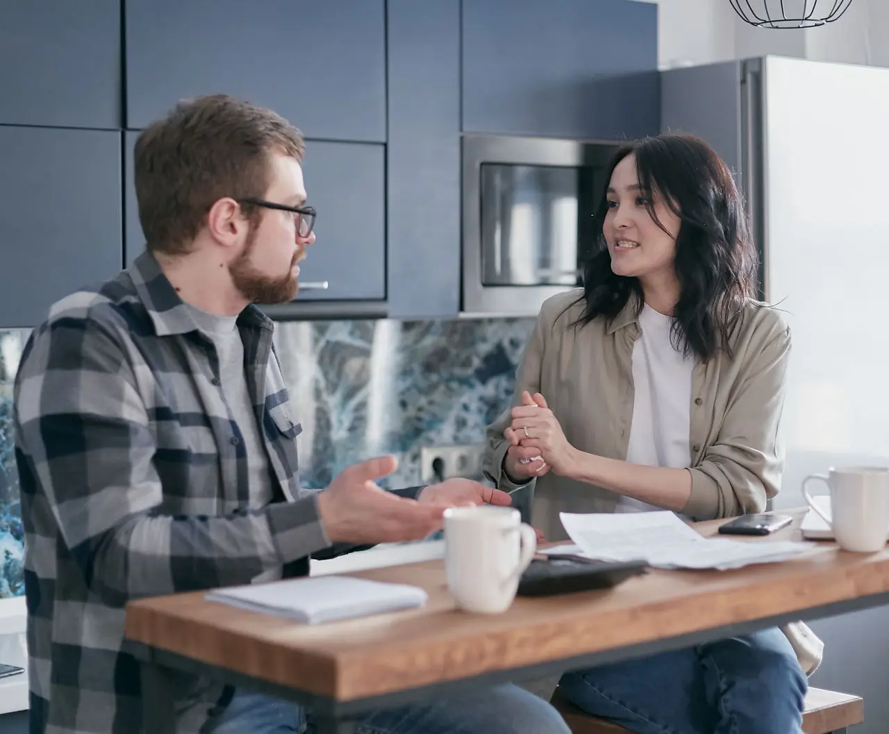 Pareja conversando de forma tranquila en la cocina mientras revisan documentos financieros